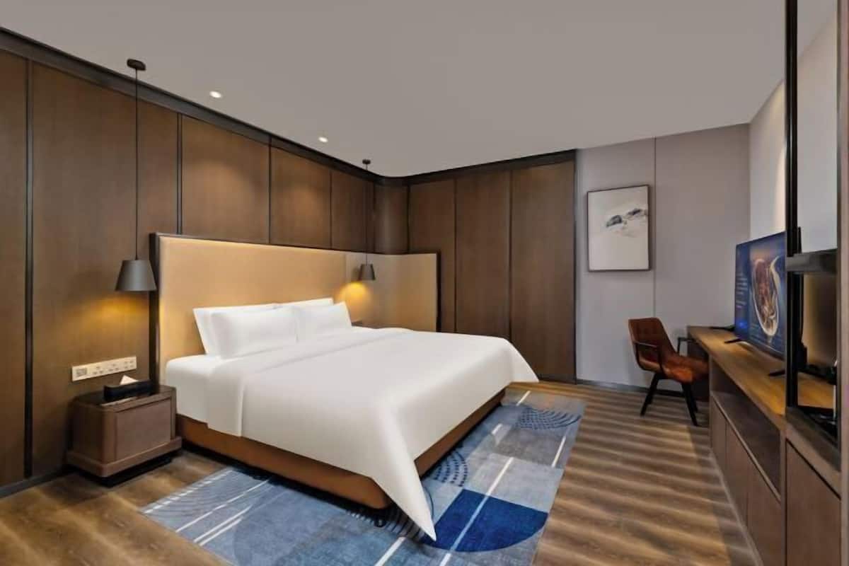 A modern hotel room with a large bed, bedside lamps, a desk with a chair, and a television.