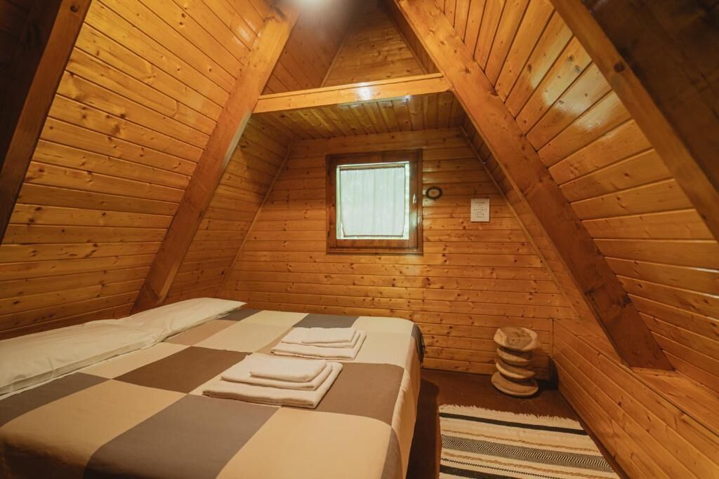 A cozy attic bedroom with wooden walls, a checkered bedspread, and a small window.