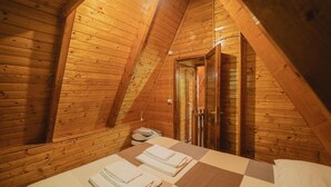 A cozy attic bedroom with wooden walls and a sloped ceiling. There is a bed with a checkered bedspread and neatly folded towels. - Accogliente chalet sul vulcano Etna, In Sicilia. Situato a quota 1500. (Nicolosi)