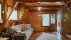 A cozy wooden cabin with a loft bedroom, a bed with pillows, a small table, and a window with curtains. - Accogliente chalet sul vulcano Etna, In Sicilia. Situato a quota 1500. (Nicolosi)