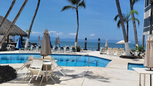 A pool area with lounge chairs and umbrellas, overlooking a beach with palm trees and a clear sky. - Depa una recamara en la playa (Bucerías)