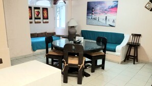 A dining area with a round glass table, black chairs, and a blue sofa. There is a painting of a lighthouse on the wall and a lamp on the table. - Depa una recamara en la playa (Bucerías)