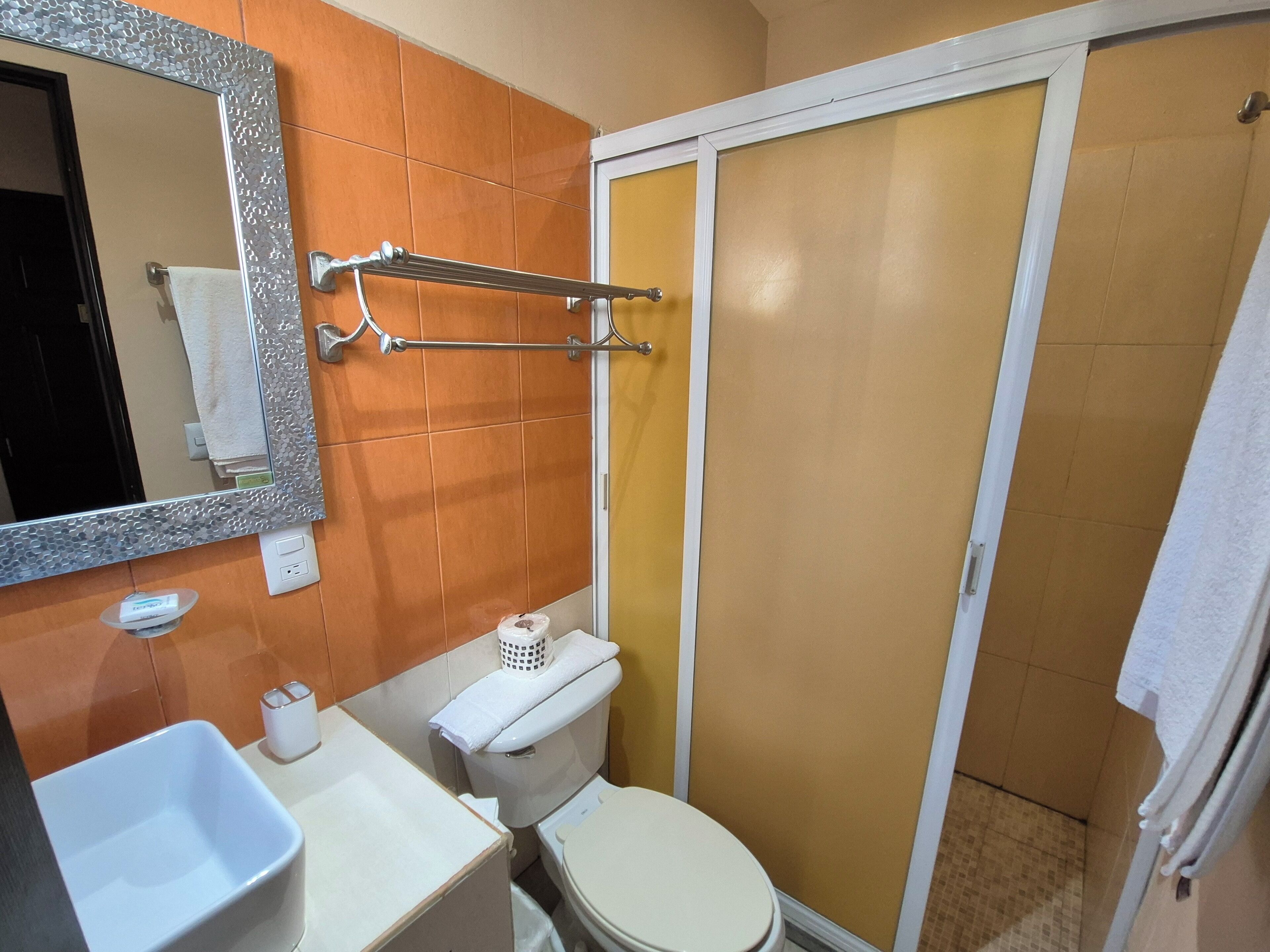 Une salle de bain comprenant des toilettes, un lavabo, un miroir et un espace douche.