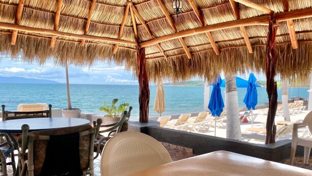 Ein Restaurant direkt am Strand, mit einem Reetdach, Außenbereich und Blick auf das Meer.