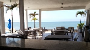 Un restaurante frente al mar con terraza, palmeras y vistas al océano.