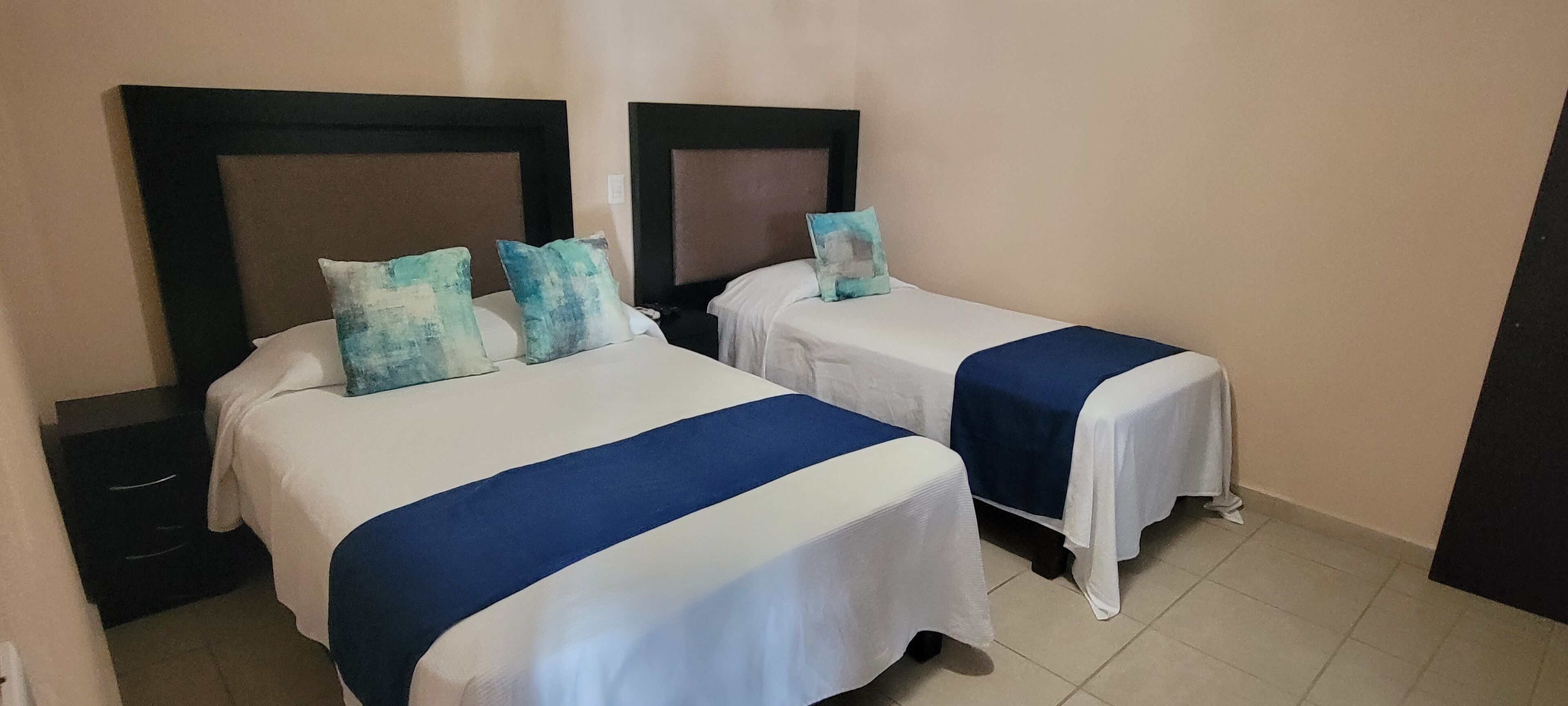 A hotel room with two beds, each with a blue bedspread and matching pillows.