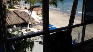 A beach view from a window with palm trees and a thatched-roof structure. - Estudio frente a la playa (Bucerías)