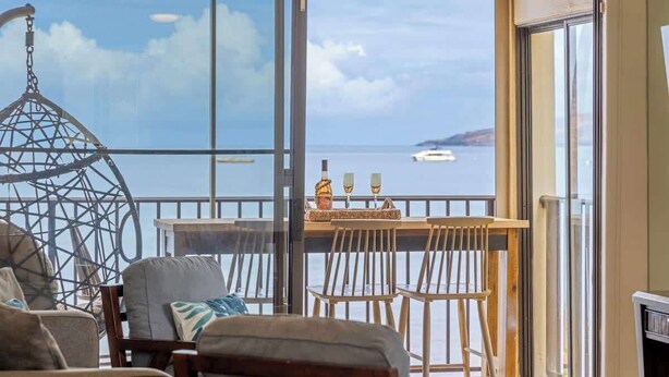 Ein Balkon mit Meerblick, einem Hängesessel und einem Tisch mit Stühlen.