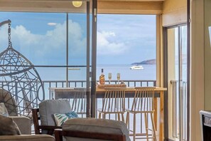 Un balcón con vista al mar, una silla colgante y una mesa con sillas.