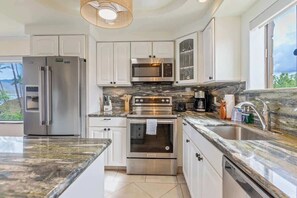 A modern kitchen with stainless steel appliances, white cabinetry, and a large window offering a view.