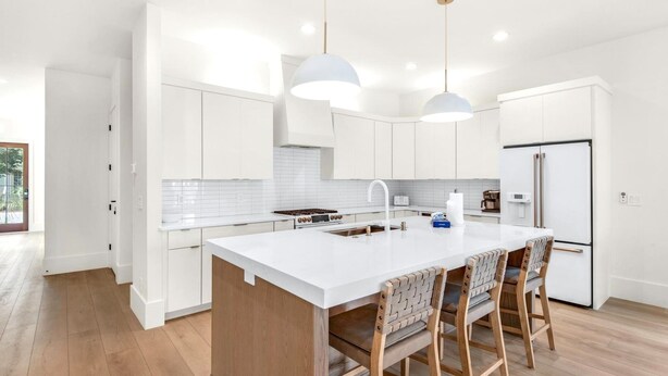 Une cuisine moderne avec des meubles blancs, un îlot central doté de tabourets et des luminaires suspendus.