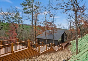 A wooden staircase leading to a cabin with a dark roof, surrounded by trees with autumn foliage.