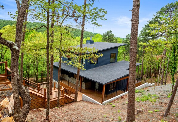 A two-story cabin with a balcony, surrounded by trees and a forested landscape.