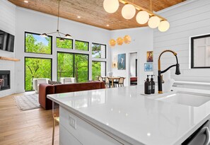 A modern kitchen with a large island, white cabinetry, and a view of the outdoors through large windows.