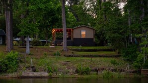 A cabin with a deck, surrounded by trees and a body of water. - Eagle`s Cove · Waterfront Amazing View, King Bed, Deck (Hemphill)