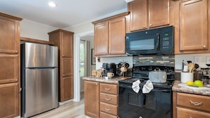 A modern kitchen with wooden cabinets, stainless steel appliances, and a tiled backsplash. - Eagle`s Cove · Waterfront Amazing View, King Bed, Deck (Hemphill)