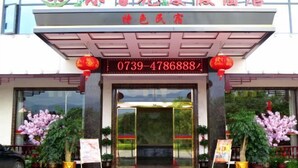 The entrance of a hotel with a red carpet, a large digital display above the door, and potted plants on either side. - Xinning Xiaobaihua Resort Hotel (Xinning)
