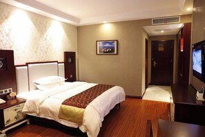 A hotel room with a bed, bedside table, TV, and a painting on the wall.