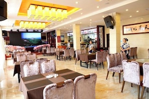 A hotel lobby with multiple dining tables and chairs, a television screen, and a bar area. - Xinning Xiaobaihua Resort Hotel (Xinning)