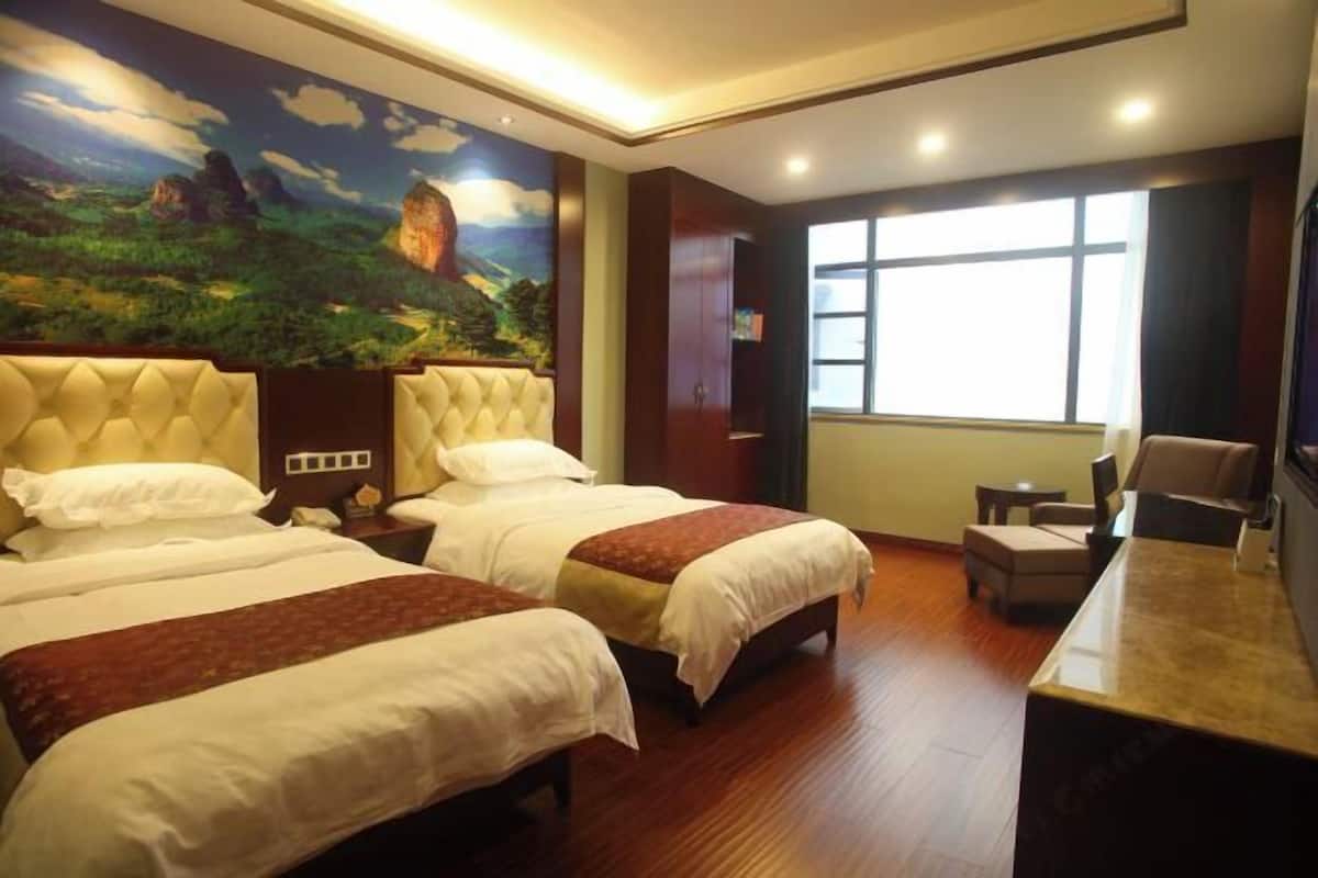 A hotel room with two beds, a large mural, a desk, and a window.