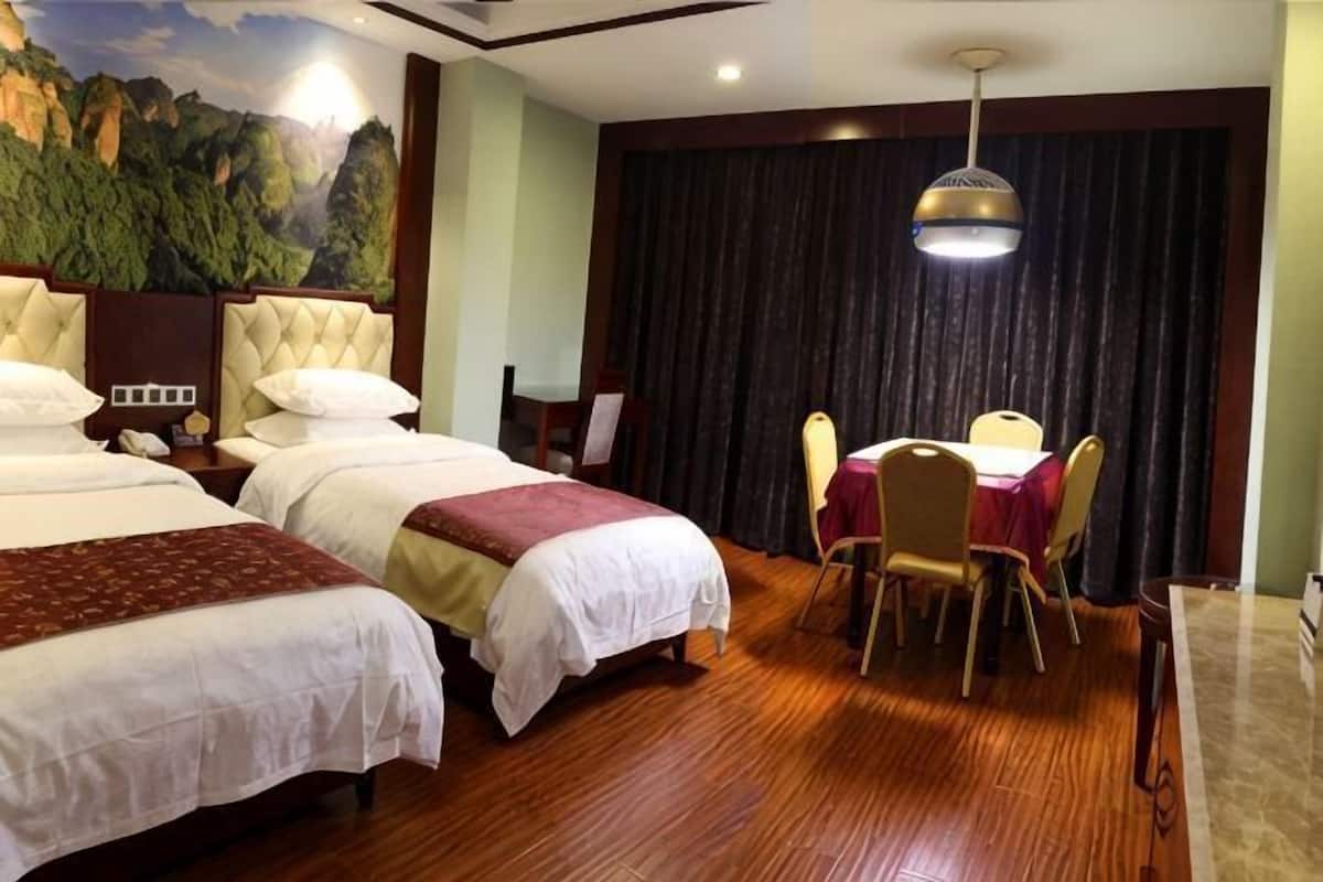 A hotel room with two beds, a dining table with chairs, a chandelier, and a mural on the wall.