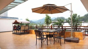 An outdoor patio with a table and chairs, a large umbrella, and a view of a mountainous landscape. - Xinning Xiaobaihua Resort Hotel (Xinning)