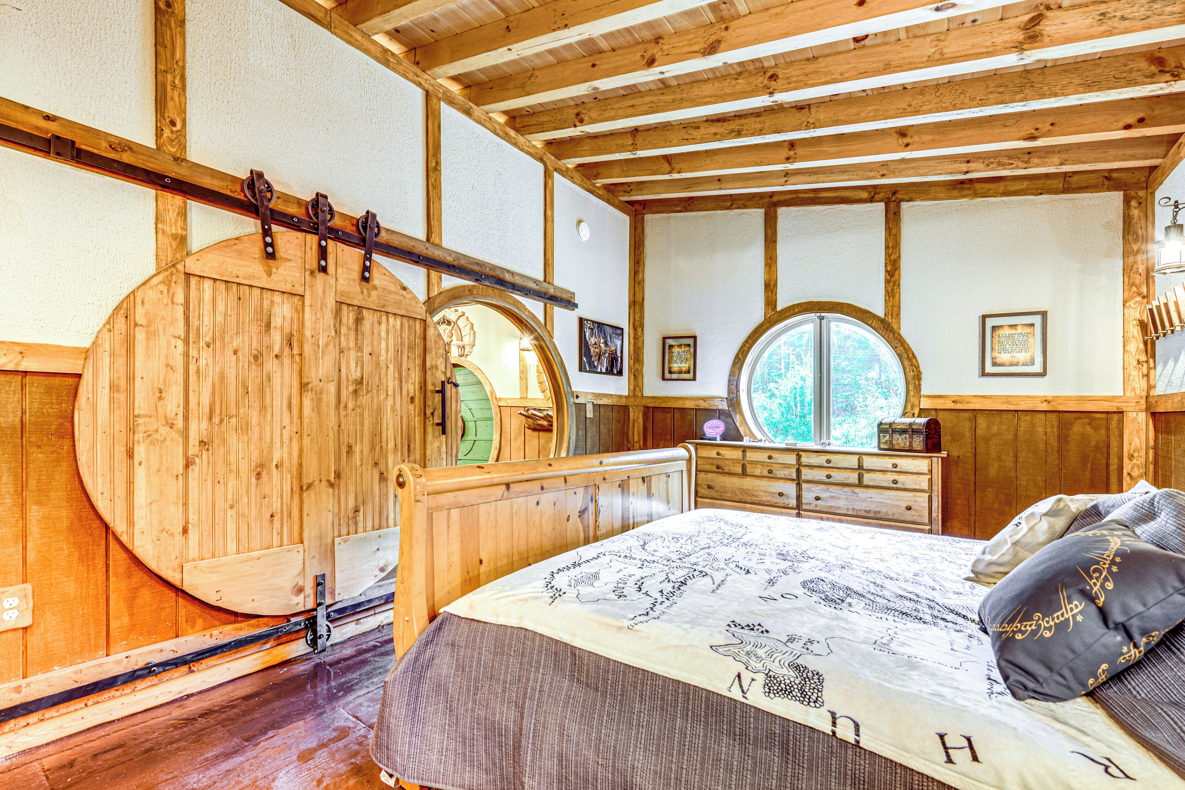 A wooden bedroom with a large round mirror, a bed with a patterned bedspread, and a dresser with a mirror.