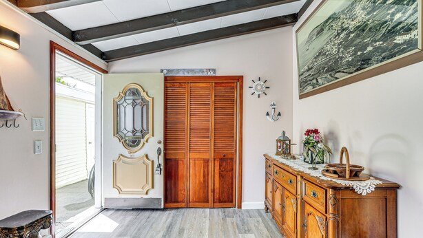 Ein Flur mit Holztür, einem Zier-Spiegel, einer Holzkabine mit Spitzen-Eckerl und einem gerahmten Bild an der Wand.