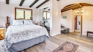 Ein Schlafzimmer mit einem großen Bett, Holzbalken, einem Spiegel und Blick zum Essbereich.