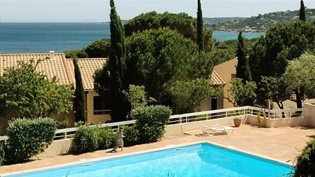 A swimming pool with a view of the sea, surrounded by trees and buildings with tiled roofs. - Beautiful apartment with pool in Sainte-Maxime (Sainte-Maxime)