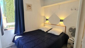 A bedroom with a bed, two bedside lamps, a window with curtains, and a wall-mounted fan. - Beautiful apartment with pool in Sainte-Maxime (Sainte-Maxime)
