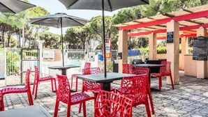 An outdoor patio with red chairs and tables, umbrellas, and a pergola structure. - St Raphaël Piscine Plage Golf Idéal Famille (Saint-Raphaël)