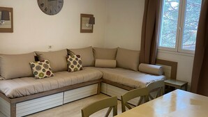 A cozy room with a sofa, a dining table, and a clock on the wall. - St Raphaël Piscine Plage Golf Idéal Famille (Saint-Raphaël)