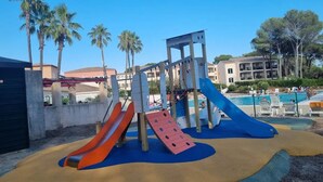 A playground with slides and climbing structures, surrounded by palm trees and a pool area. - St Raphaël Piscine Plage Golf Idéal Famille (Saint-Raphaël)