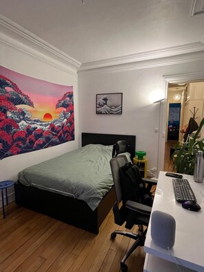 A bedroom with a bed, desk, chair, and a wall with two paintings.