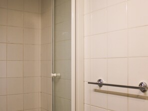 Une salle de bain avec des carreaux blancs, une porte de douche en verre et un porte-serviettes en métal.