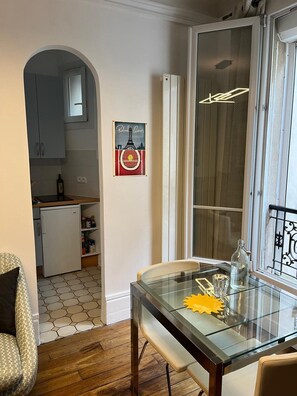 Une cuisine compacte comprenant un réfrigérateur, une table à manger avec des chaises et une fenêtre ornée d’une grille métallique décorative.