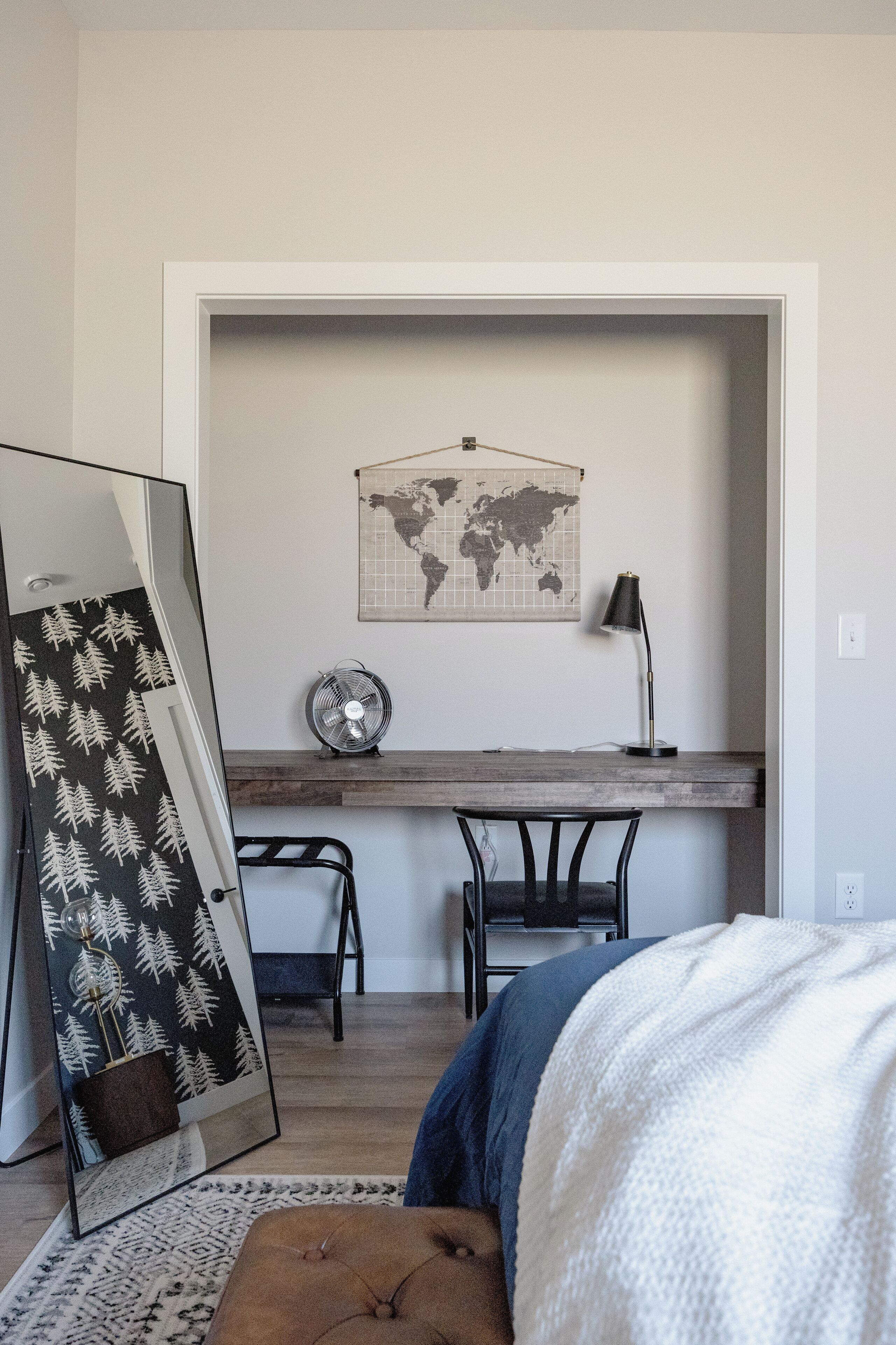 A bedroom with a bed, a desk, a chair, a map on the wall, and a mirror.