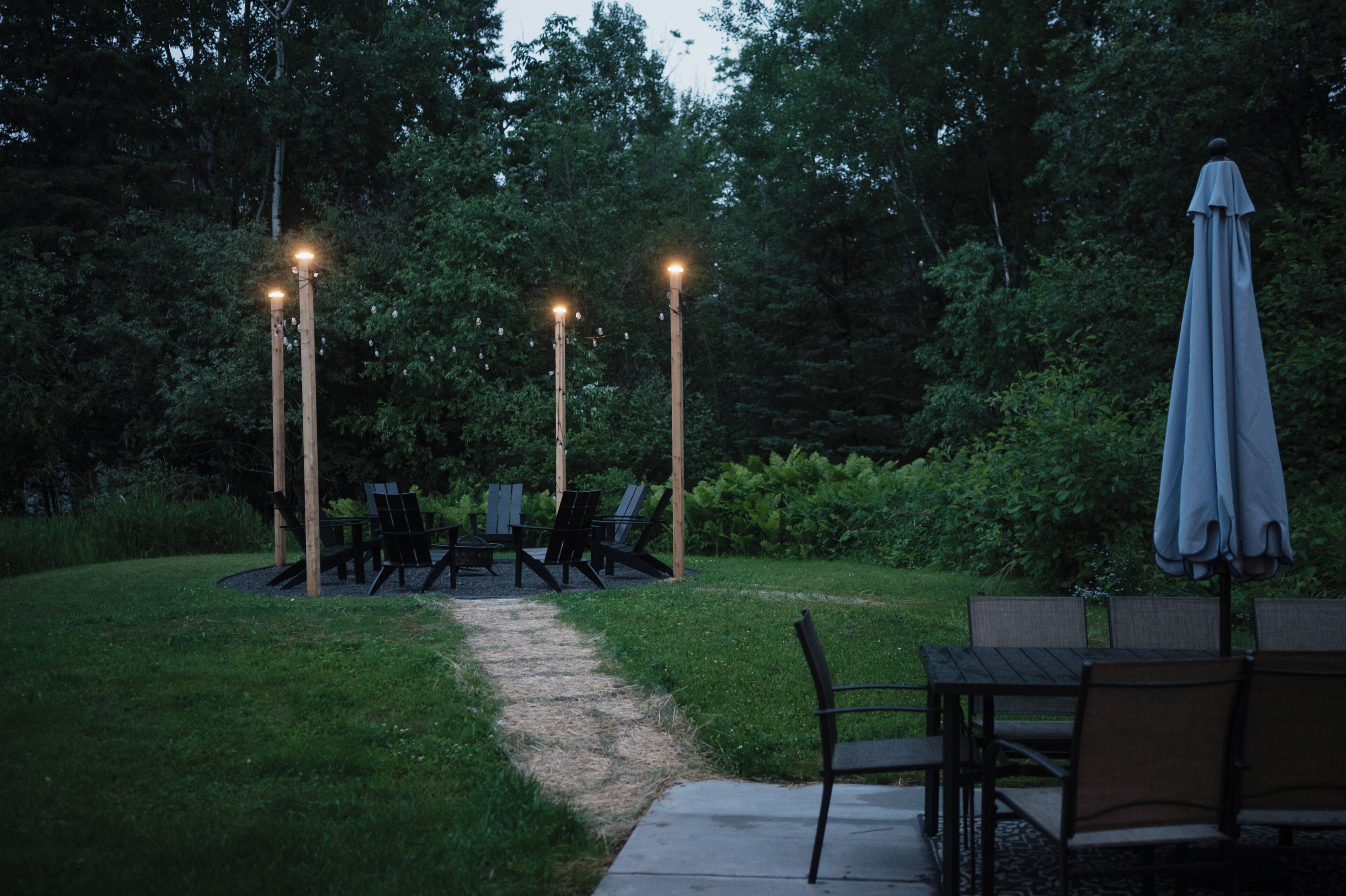 An outdoor patio area with a pathway leading to a seating arrangement, surrounded by greenery.