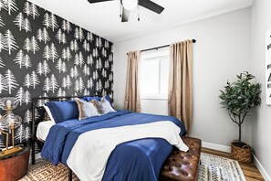 A bedroom with a bed, a ceiling fan, a window with curtains, a potted plant, and a wall with a tree pattern. - Walking distance to Pike Lake beach, hot tub & game room, pet friendly (Duluth)