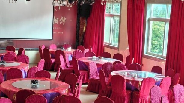 Un salón de conferencias con mesas y sillas redondas, una pantalla de proyector y cortinas rojas.
