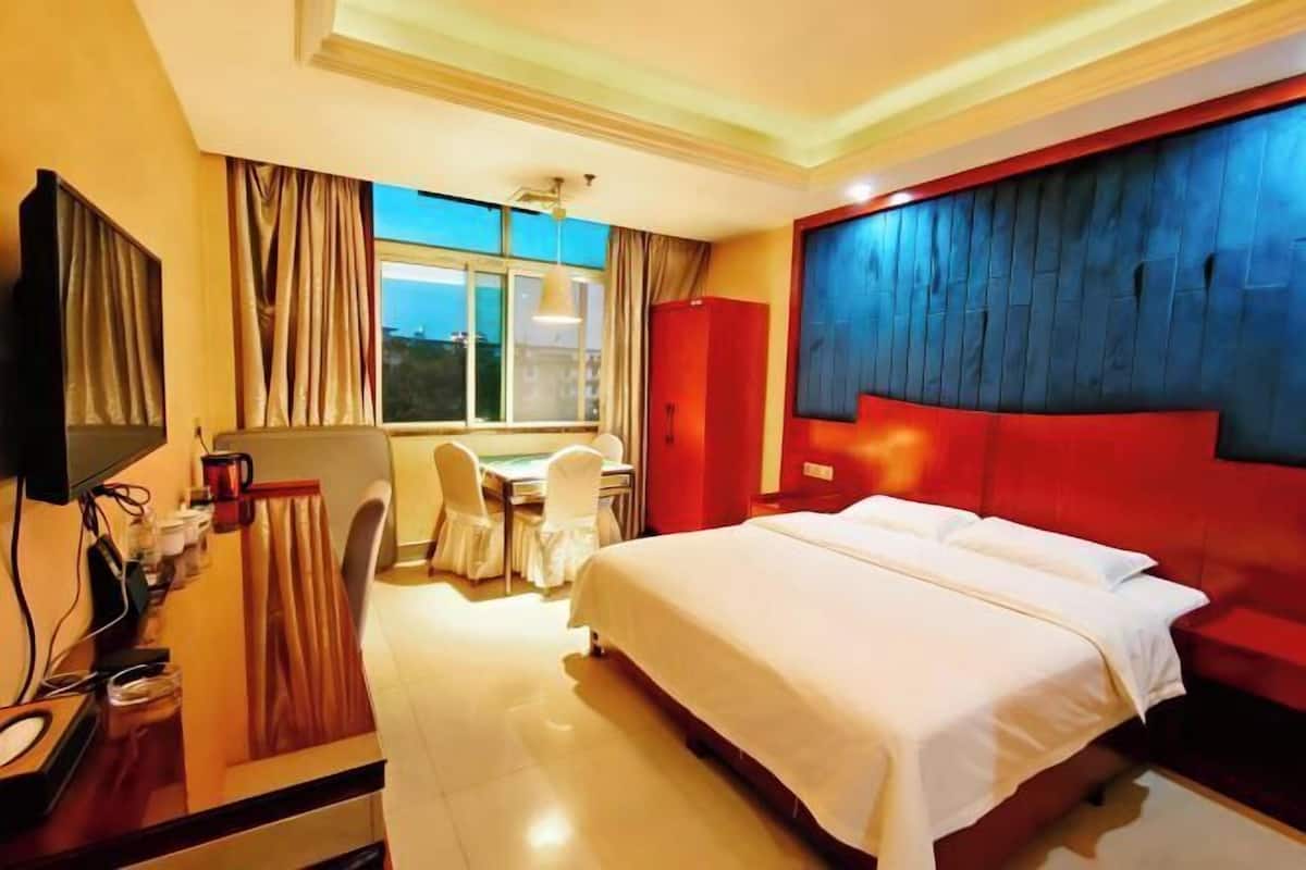 Een hotelkamer met een bed, een bureau met stoel, een televisie en een raam met gordijnen.