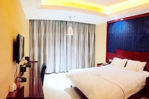 Une chambre d’hôtel avec un lit, un bureau avec une télévision, un miroir et une fenêtre avec des rideaux.