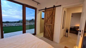 Un dormitorio con una cama grande, una puerta corrediza estilo granero y vistas a un paisaje verde a través de amplias ventanas.