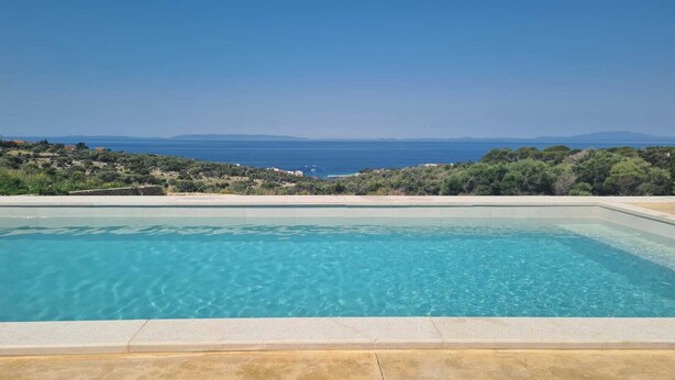 A rectangular swimming pool with clear blue water, surrounded by a concrete deck, and overlooking a coastal landscape with hills and a view of the sea. - Villa SOL Insulam (Novalja)