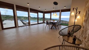 A spacious room with large windows offering a view of a pool and hills. There is a dining area with a table and chairs, and a bar with bottles and glasses. - Villa SOL Insulam (Novalja)