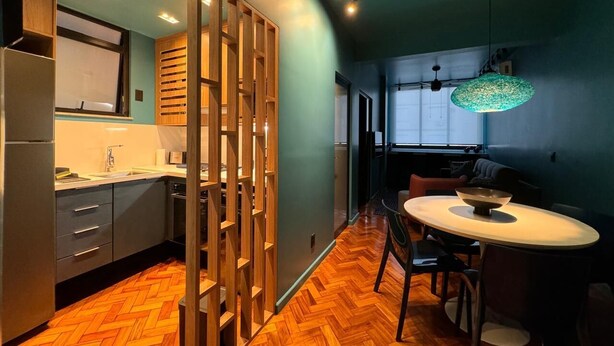 Una cocina moderna con suelo de madera en espiga, un comedor con una mesa redonda y una lámpara colgante verde.