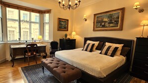 Une chambre avec un grand lit, un bureau et une chaise. Il y a une fenêtre avec des rideaux, un lustre et des lampes fixées au mur.