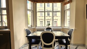 Un coin repas avec une table et des chaises, une fenêtre donnant sur des immeubles et un téléviseur fixé au mur.