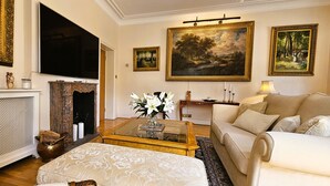 Un salon avec une cheminée, un canapé, une table basse et des tableaux accrochés au mur.